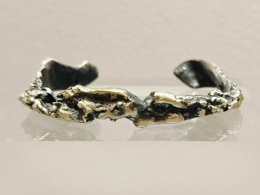 Pulsera artesanal en plata mate y negro óxido con diseño texturizado e irregular, destacando su elegancia y estilo rústico