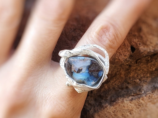 Primer plano del anillo plateado con la piedra ópalo Boulder es en un dedo.